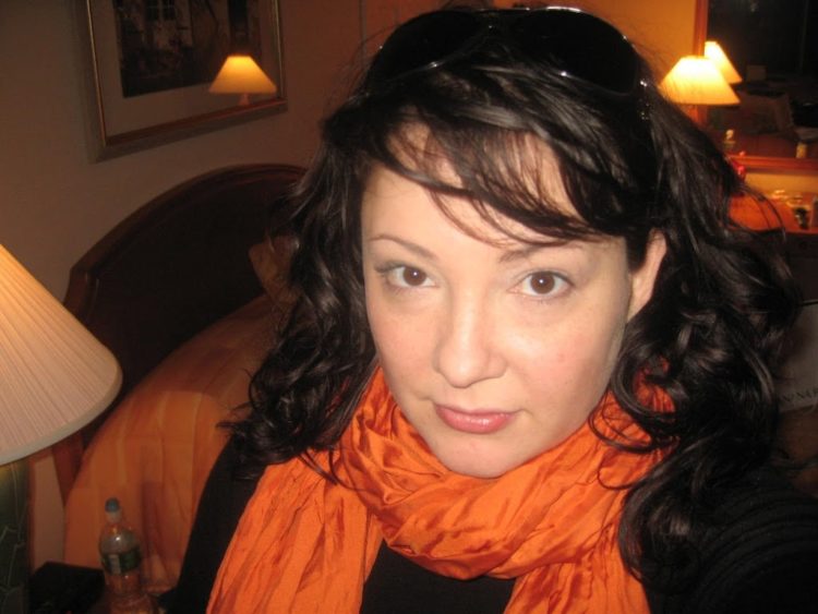Alison Gary with her dark brown hair pulled back with black sunglasses, an orange crinkle silk scarf looped around her neck