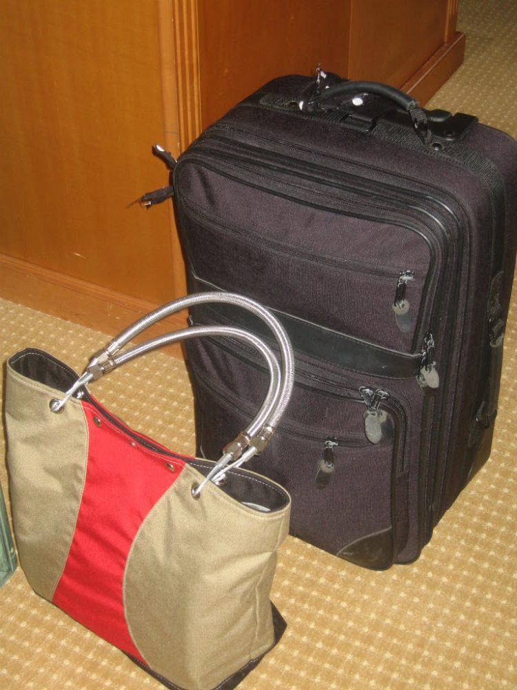 a black rolling suitcase next to a tan and red totebag from HARDWARE Handbags