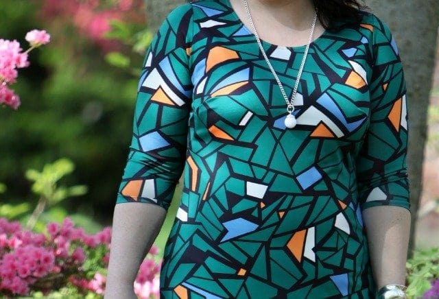 a petite size 14 woman in a green mosaic print bracelet sleeve length sheath, wearing black pumps and holding a black leather tote bag