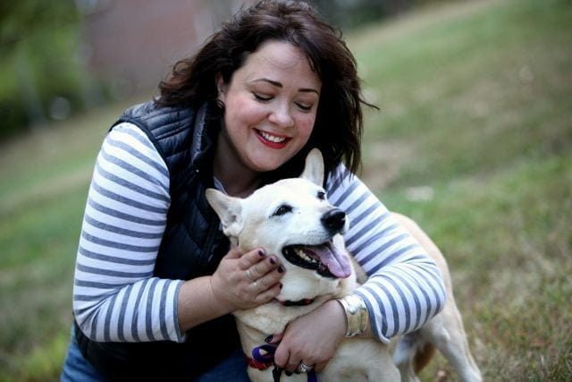 woman hugging a blonde dog who looks to be smiling