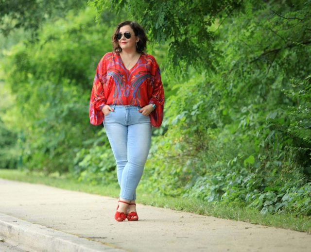 Alison Gary of Wardrobe Oxygen wearing a red printed chiffon blouse from Free People with light wash ankle jeans, carrying a black leather tote bag and wearing red suede platform heeled sandals