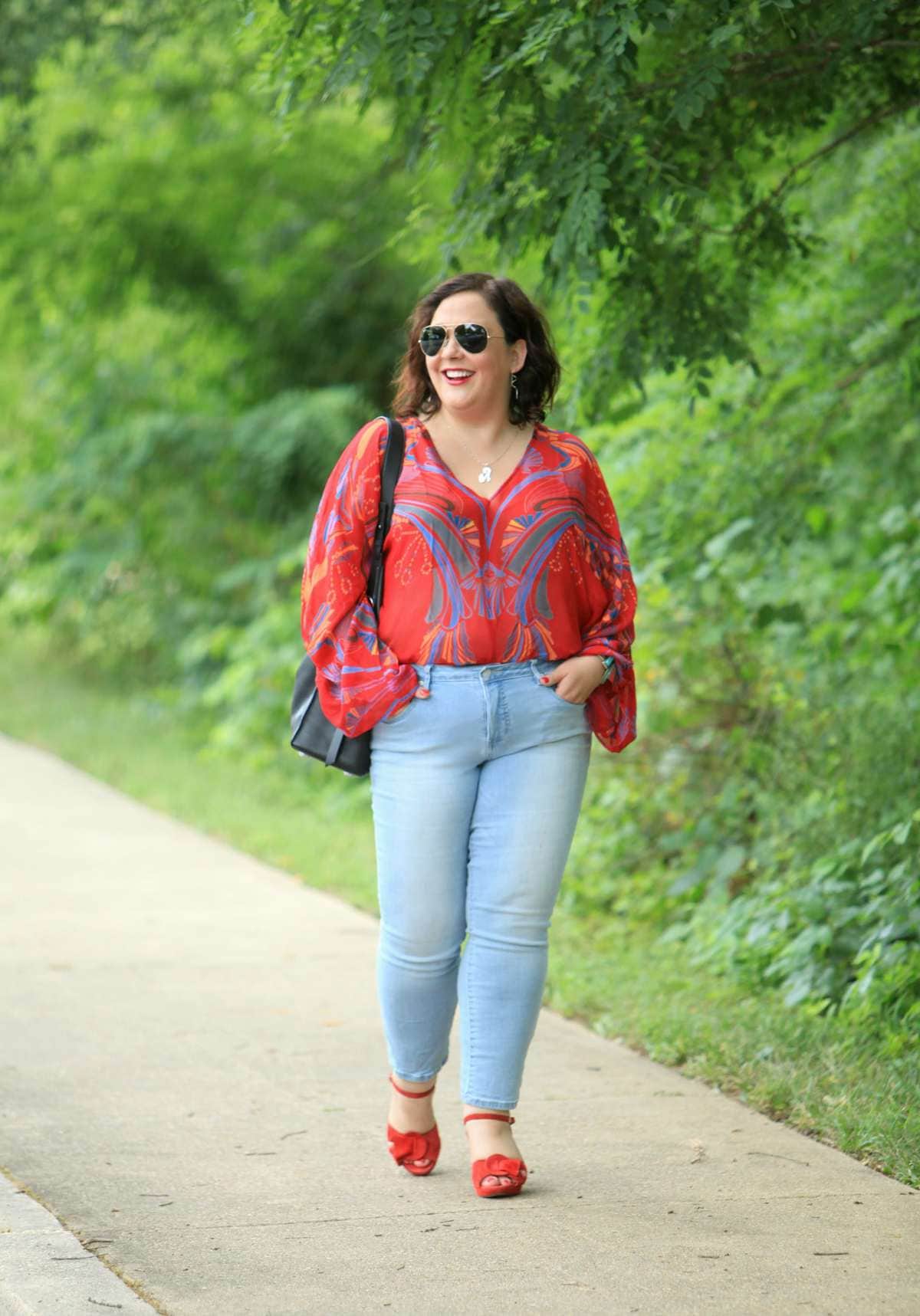 Alison Gary of Wardrobe Oxygen wearing a red printed chiffon blouse from Free People with light wash ankle jeans, carrying a black leather tote bag and wearing red suede platform heeled sandals