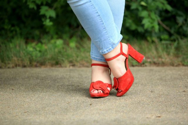 Picture of feet, ankles crossed. The legs are in light wash ankle length jeans, on the feet are red suede ankle strap block heel platform sandals.
