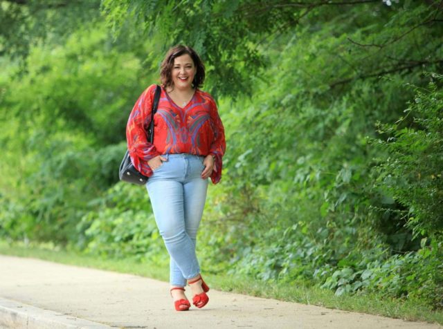 Alison Gary of Wardrobe Oxygen wearing a red printed chiffon blouse from Free People with light wash ankle jeans, carrying a black leather tote bag and wearing red suede platform heeled sandals