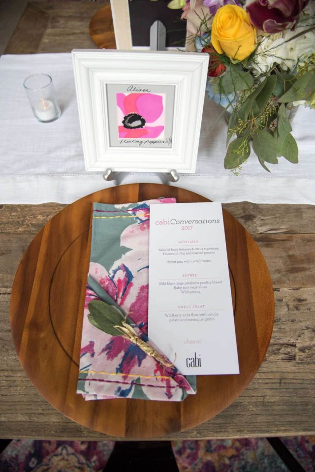 photo of a wood platter with a menu on top of it. Behind it is a square picture frame with a poppy painting inside, and the name Alison written in script above the poppy