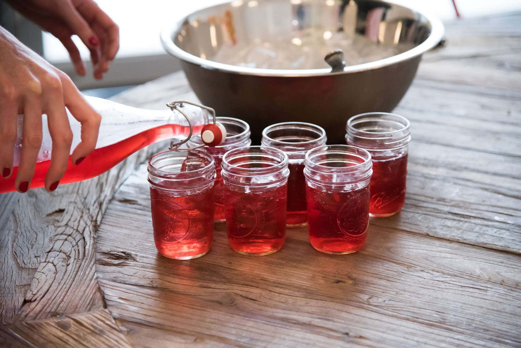 hibiscus collins cocktail being poured from a bottle into mason jars