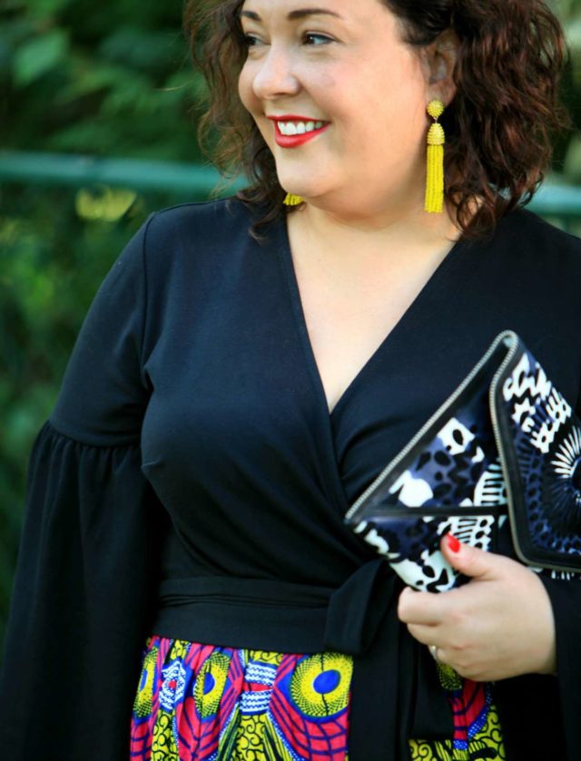 Wardrobe Oxygen in Baublebar tassel earrings, an ELOQUII wrap top, and Rebecca Minkoff clutch