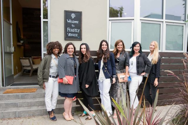 Seven bloggers standing outside a building with a sign on it that says Welcome to Feastly. 