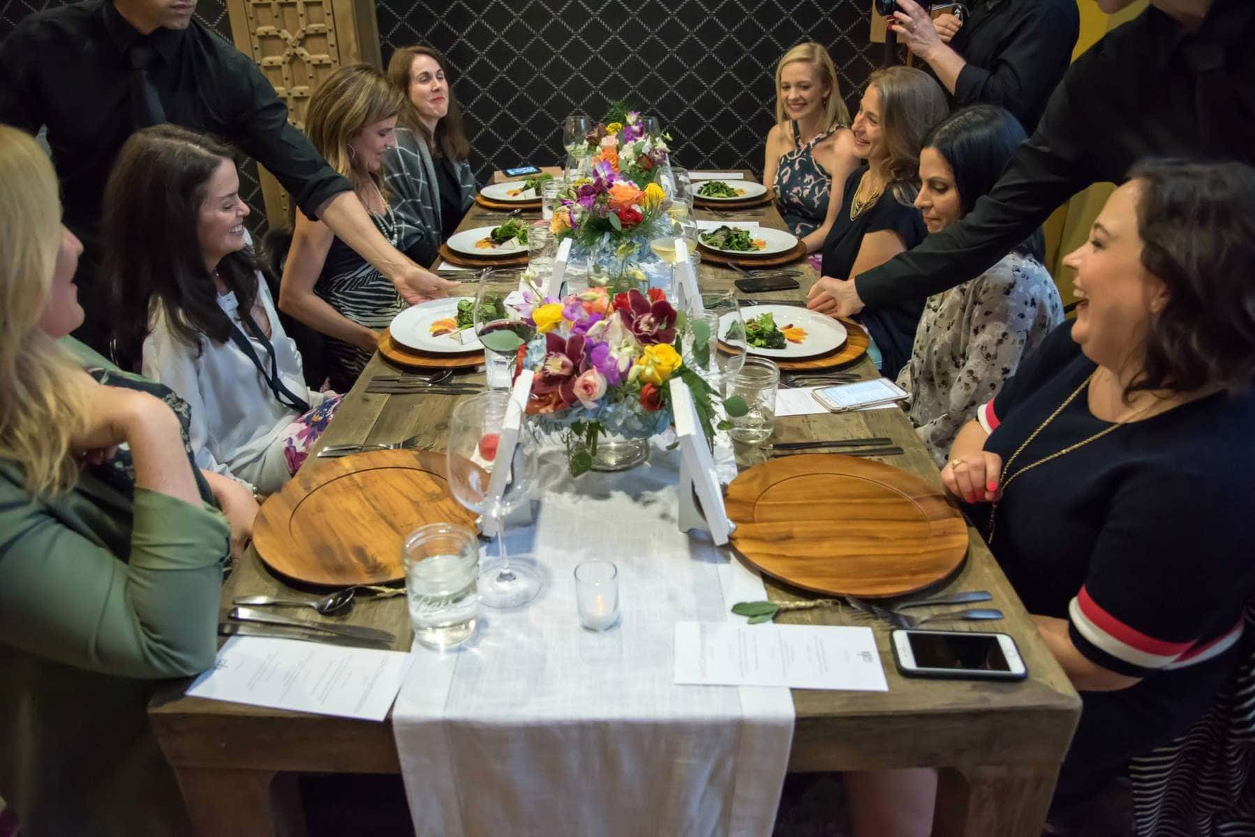 a table with eight women sitting at it laughing and speaking