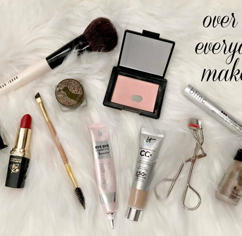 Photo of makeup laid out on. sheepskin rug. An opened compact of blush, tube of lipstick, tubes of concealer and CC cream and mascara. An eyelash curler, a few brushes, a pot of eyebrow color and jar of eyelid concealer.