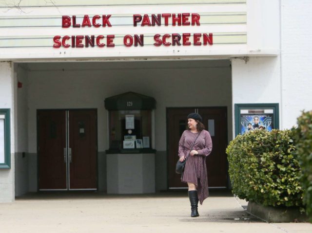 Woman in a red stripe long sleeve asymmetrical dress with a black beret, black round crossbody bag, and black knee-high boots. She is standing in front of the Greenbelt Cinema in Greenbelt, MD.