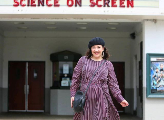 Woman in a red stripe long sleeve asymmetrical dress with a black beret, black round crossbody bag, and black knee-high boots. She is standing in front of the Greenbelt Cinema in Greenbelt, MD.