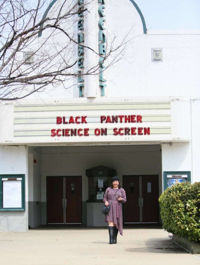 Woman in a red stripe long sleeve asymmetrical dress with a black beret, black round crossbody bag, and black knee-high boots. She is standing in front of the Greenbelt Cinema in Greenbelt, MD.