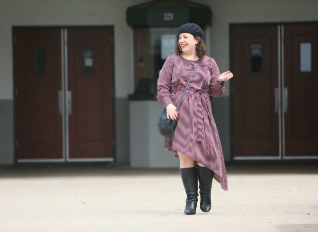 Woman in a red stripe long sleeve asymmetrical dress with a black beret, black round crossbody bag, and black knee-high boots. She is standing in front of the Greenbelt Cinema in Greenbelt, MD.