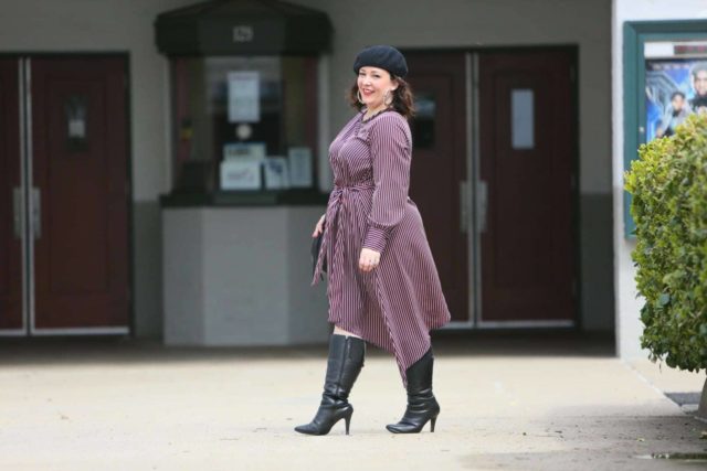 Woman in a red stripe long sleeve asymmetrical dress with a black beret, black round crossbody bag, and black knee-high boots. She is standing in front of the Greenbelt Cinema in Greenbelt, MD.