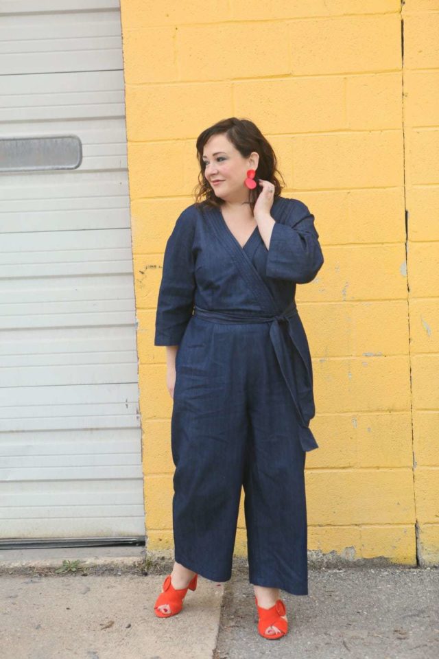 Wardrobe Oxygen in a denim wrap style jumpsuit from ELOQUII with orange suede Ann Taylor heeled sandals and red lucite statement earrings - ELOQUII Denim Jumpsuit styled by popular Washington DC petite fashion blogger, Wardrobe Oxygen