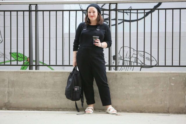 Universal Standard black overalls with a black cashmere sweater, EVA Birkenstocks, and the Dagne Dover Dakota backpack on Wardrobe Oxygen