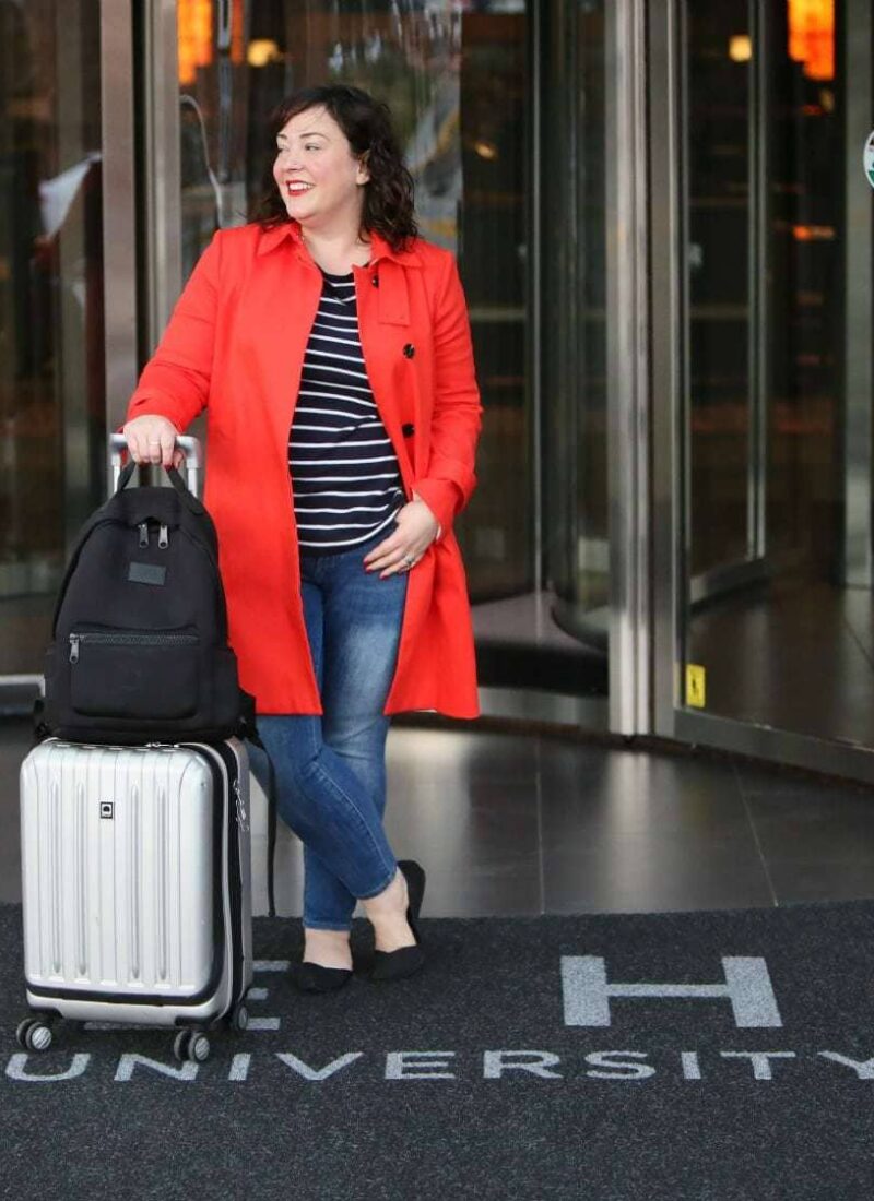 Wardrobe Oxygen in a red orange trench from Banana Republic with Talbots striped top, Banana Republic ankle jeans, Rothy's flats, Dagne Dover backpack and Delsey spinner suitcase