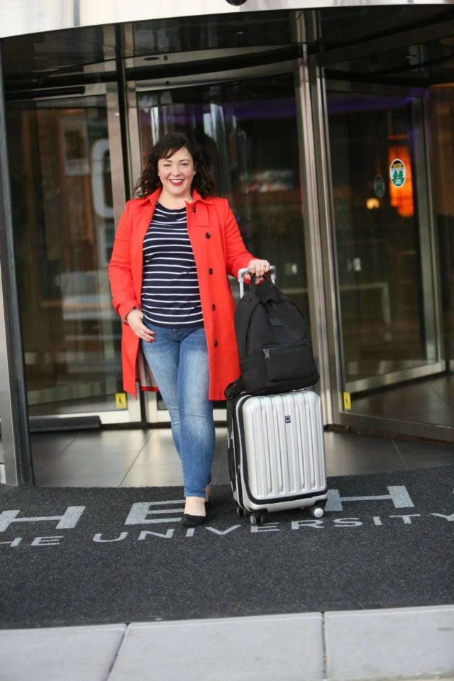 Wardrobe Oxygen in a red orange trench from Banana Republic with Talbots striped top, Banana Republic ankle jeans, Rothy's flats, Dagne Dover backpack and Delsey spinner suitcase