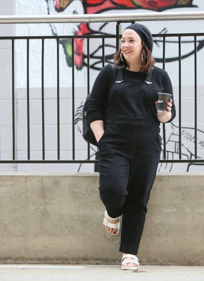Universal Standard black overalls with a black cashmere sweater, EVA Birkenstocks, and the Dagne Dover Dakota backpack on Wardrobe Oxygen