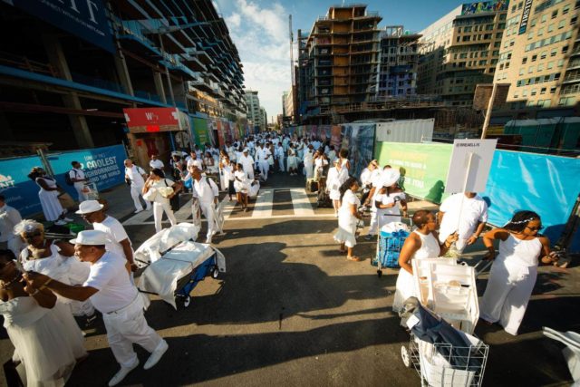 Image of individuals in white with supplies for a pop-up dinner standing in lin to enter Nationals Stadium in Washington DC