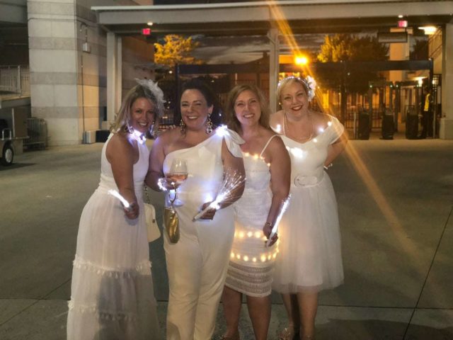 Four women in white dresses holding battery operated fairy lights with fairy lights woven through their dresses.