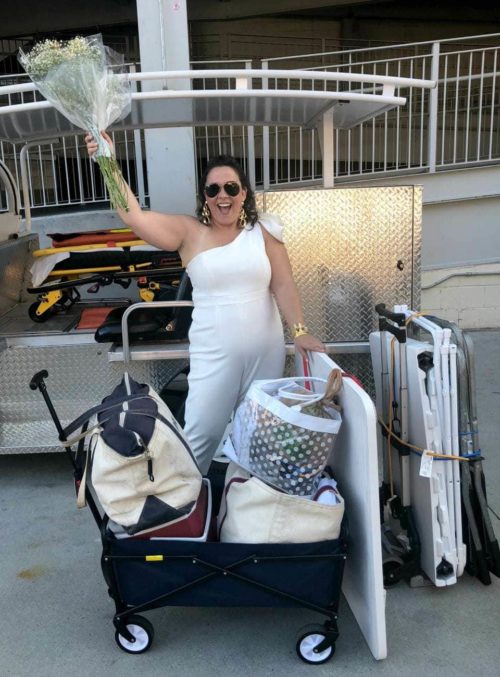 woman at Diner en Blanc wearing a white jumpsuit with a rolling cart and handtruck holding tables and chairs