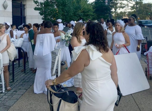 People dressed in white standing in a crowd with carts holding supplies for Dîner en Blanc