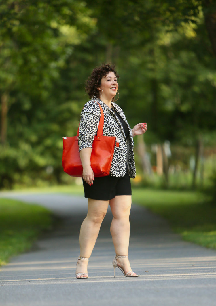 Alison wearing a leopard print blazer with a black tee and black shorts carrying an orange Clare V tote