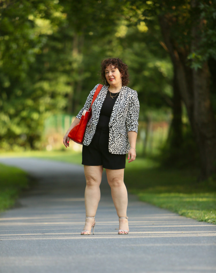 Alison wearing a leopard print blazer with a black tee and black shorts carrying an orange Clare V tote