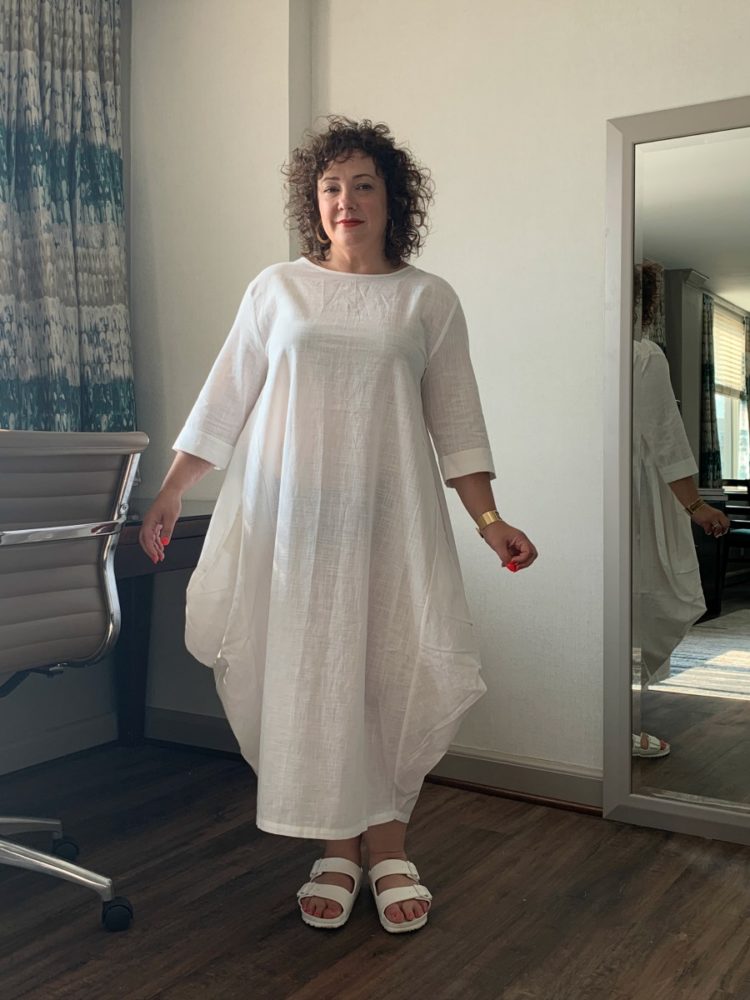 Alison Gary of Wardrobe Oxygen standing in an ankle-length loose cotton dress with elbow length sleeves. This is for a DUBGEE by Whoopi review of the clothing line