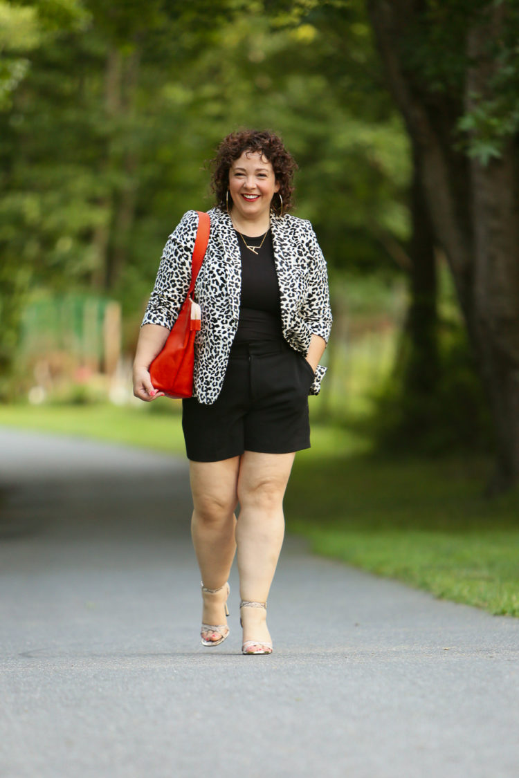 Alison wearing a leopard print blazer with a black tee and black shorts carrying an orange Clare V tote