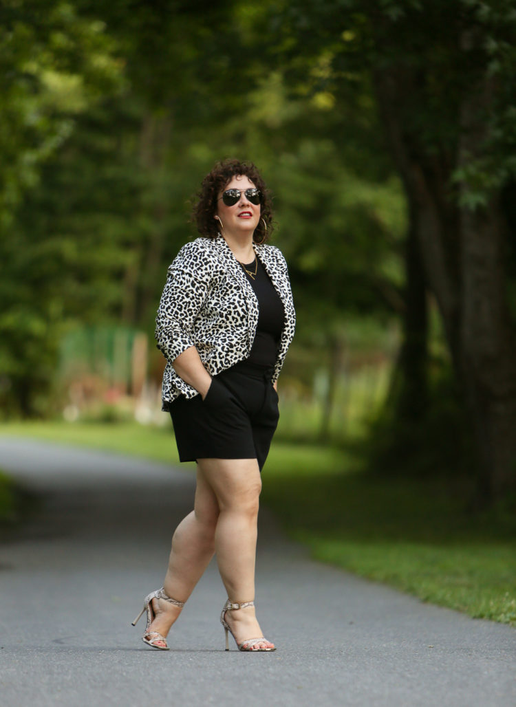 Alison wearing a leopard print blazer with a black tee and black shorts carrying an orange Clare V tote