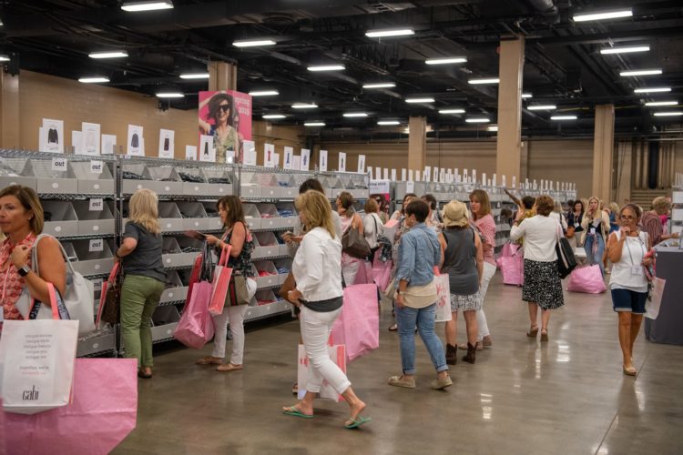 women shopping in a warehouse like location carrying large pink tote bags