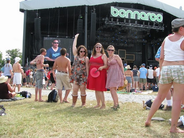 three women standing in front of a music stage at bonnaroo