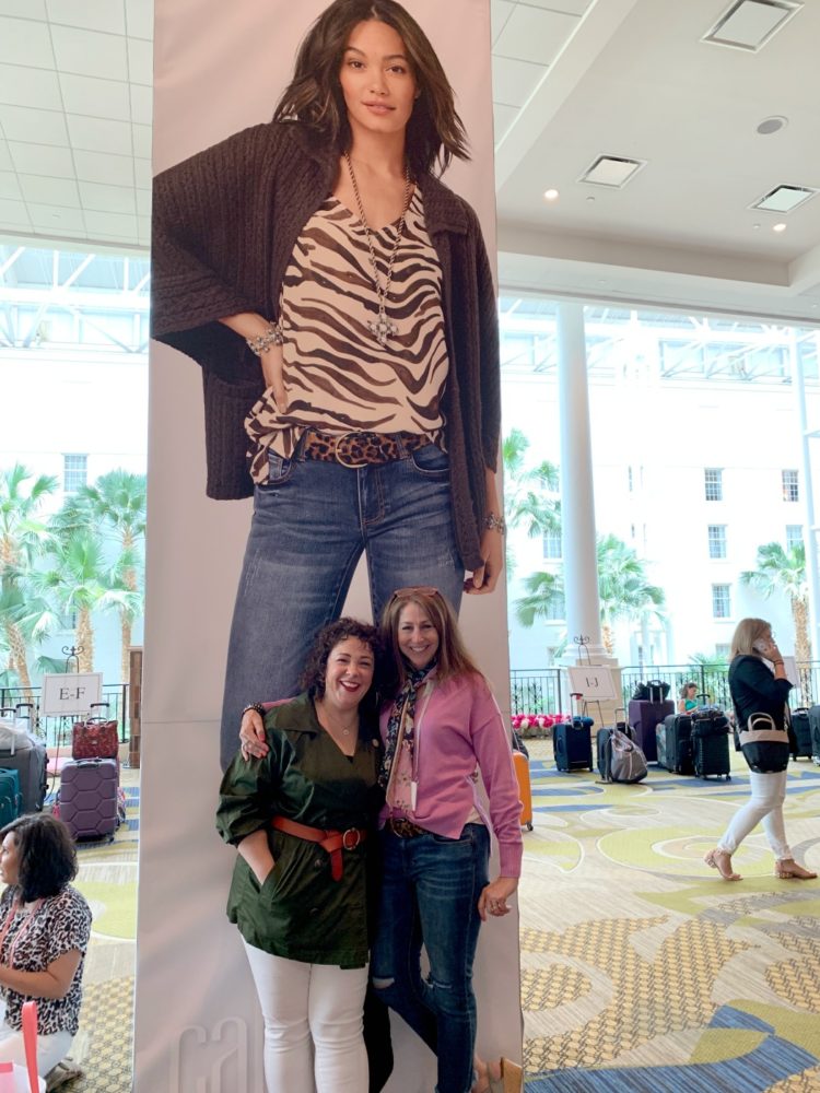 two women standing in front of a poster marketing cabi