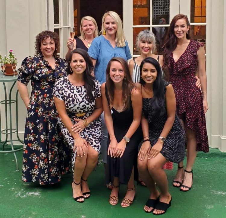 Eight women at the City Tavern Club on the terrace grouped together and smiling for the camera