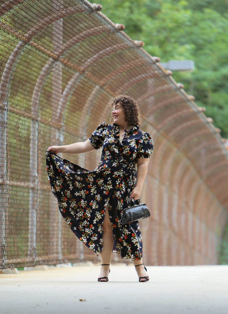 Woman in a navy floral midi dress holding up the edge of the dress to show the volume, smiling and looking away