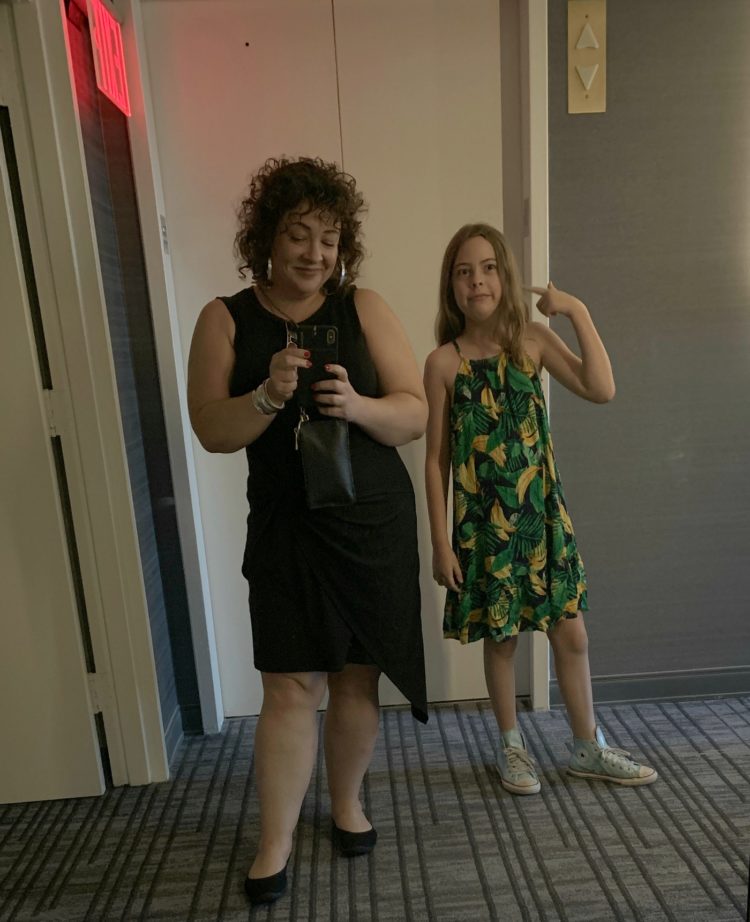 woman in black dress and flat shoes taking a mirror selfie