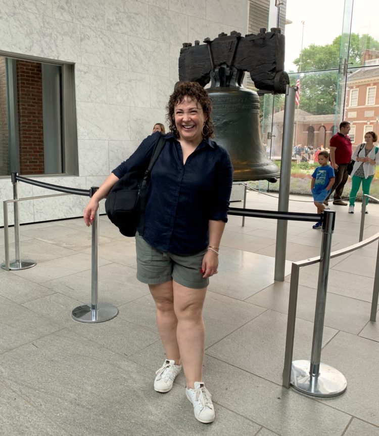 woman in navy linen shirt and olive chino shorts standing in front of the Liberty Bell