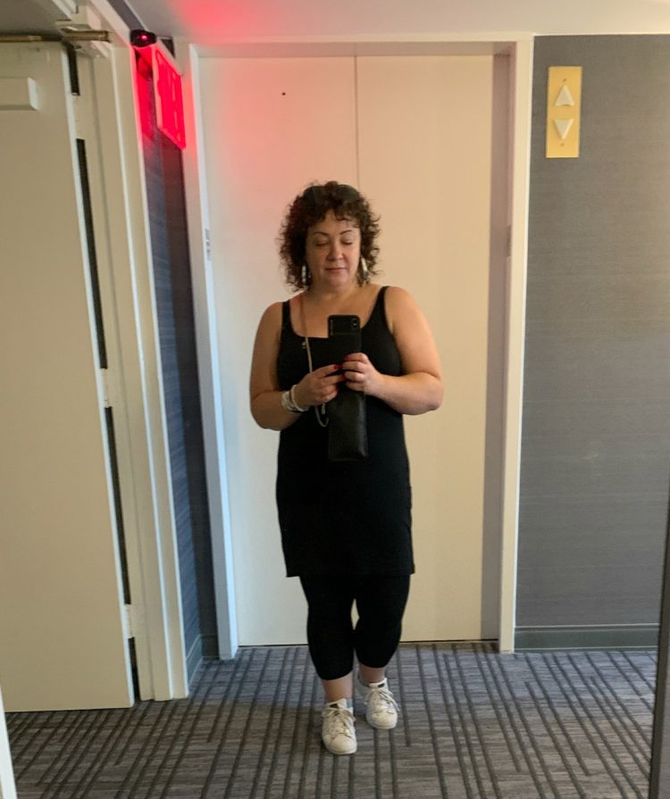 woman in black tank dress and leggings taking a mirror selfie