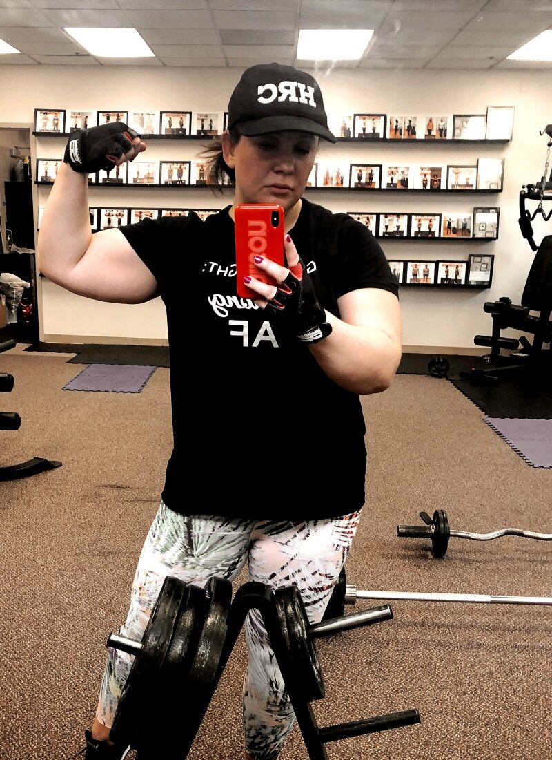 woman taking mirror selfie with one arm flexed to show her biceps