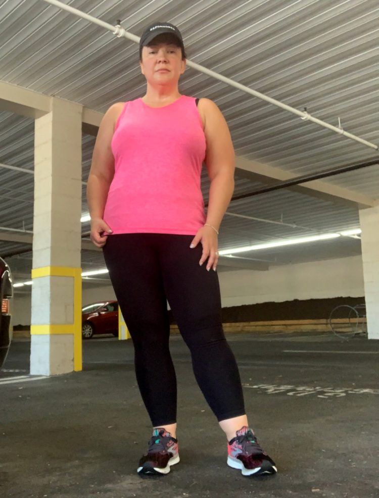 woman in pink activewear sleeveless top and black leggings standing and staring at the camera