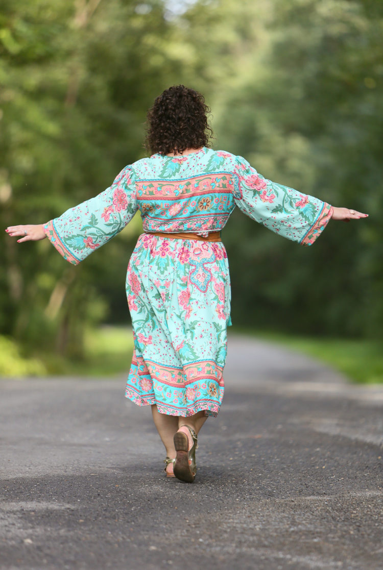 back view of a woman in a light green floral boho inspired midi length dress