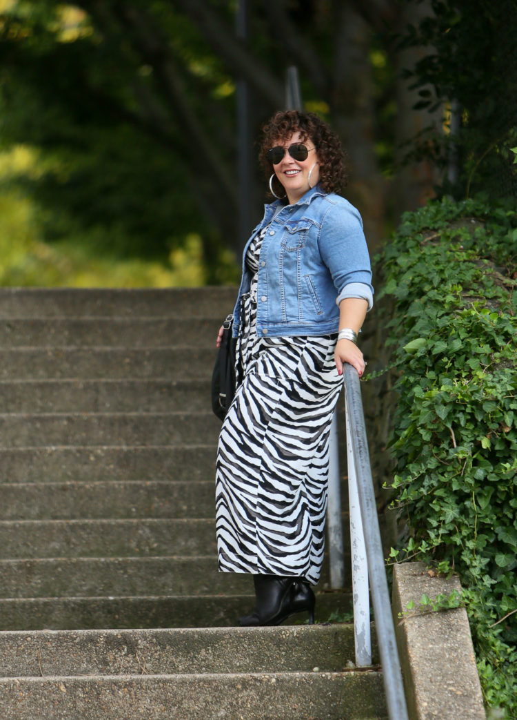 Styling a summer jumpsuit for fall - tips on how to do this successfully by Wardrobe Oxygen who is wearing a zebra print Banana Republic jumpsuit with a denim jacket and black ankle booties by Clark's and carrying a Rough & Tumble handbag in black leather.