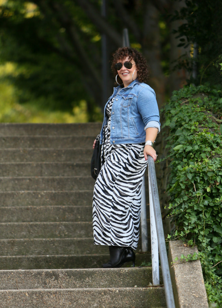 Styling a summer jumpsuit for fall - tips on how to do this successfully by Wardrobe Oxygen who is wearing a zebra print Banana Republic jumpsuit with a denim jacket and black ankle booties by Clark's and carrying a Rough & Tumble handbag in black leather.