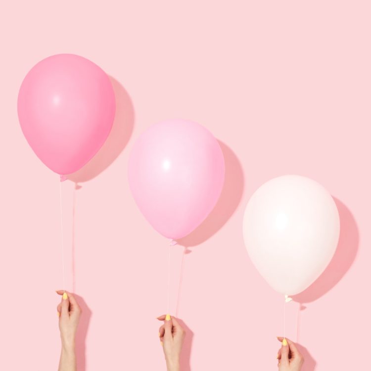 three hands in front of a pink background each holding a balloon