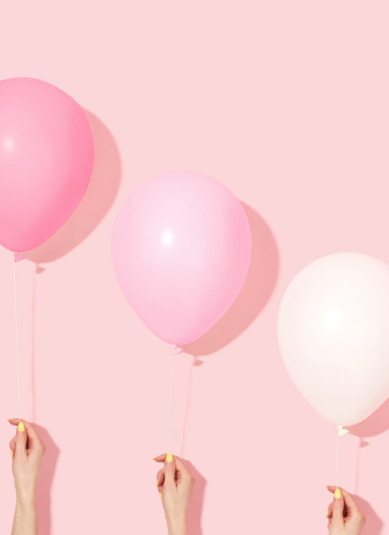 three hands in front of a pink background each holding a balloon