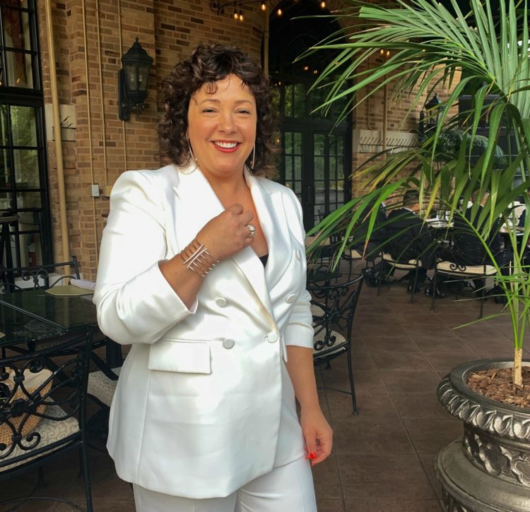 woman in a white pantsuit wearing a silver and CZ cuff bracelet and earrings