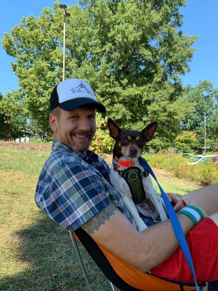man sitting in a camp chair smiling while holding a small dog